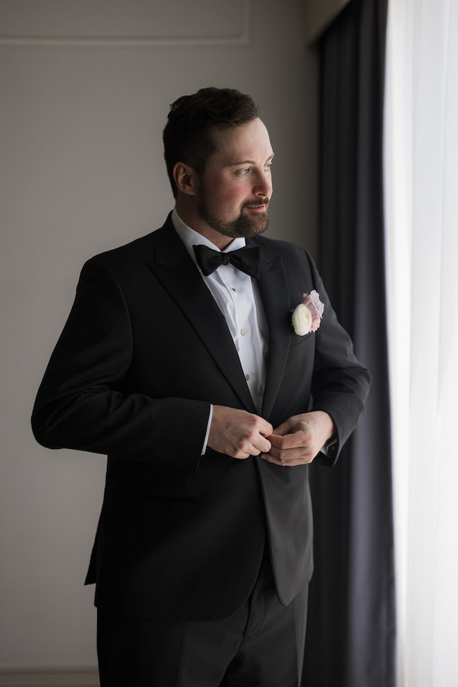 Groom buttoning up suit with white and light pink corsage.