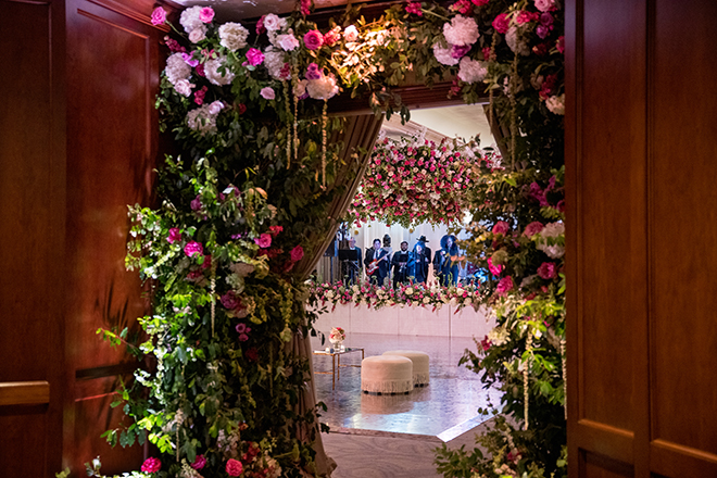 Florals and greenery decorate the entrance into the pink and brown wedding reception.