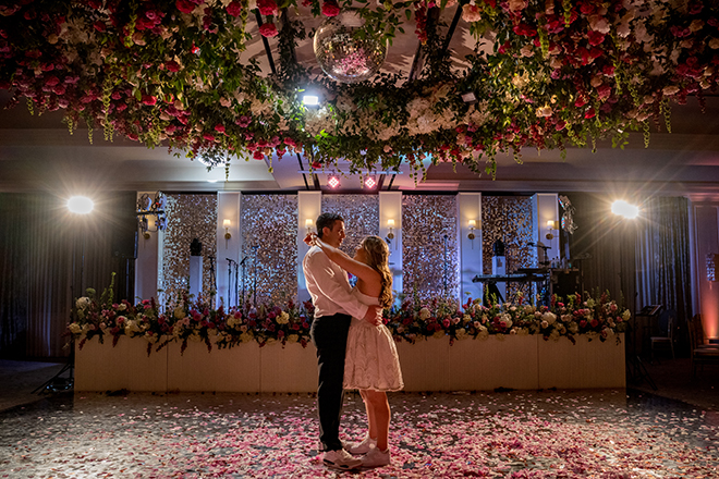 The bride and groom share a private last dance at their wedding reception under a floral installation.