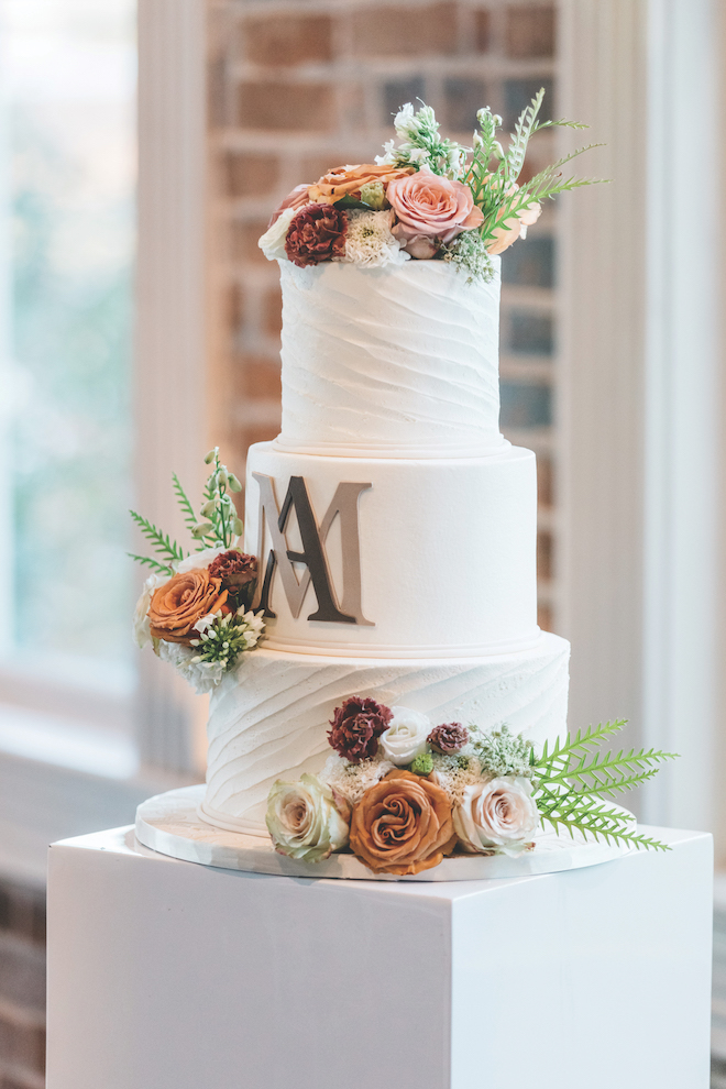 3 tier white cake with warm toned florals with an A & M on it.