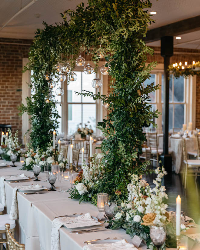 Greenery arch with string lights dangling down on wedding party table for Station 3 wedding.