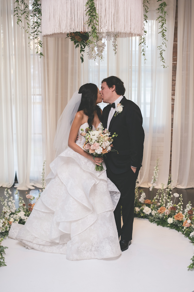 Newlyweds kissing surrounded by florals at the altar.