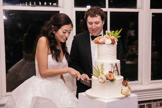 Bride and groom cutting into 3 tier floral wedding cake.