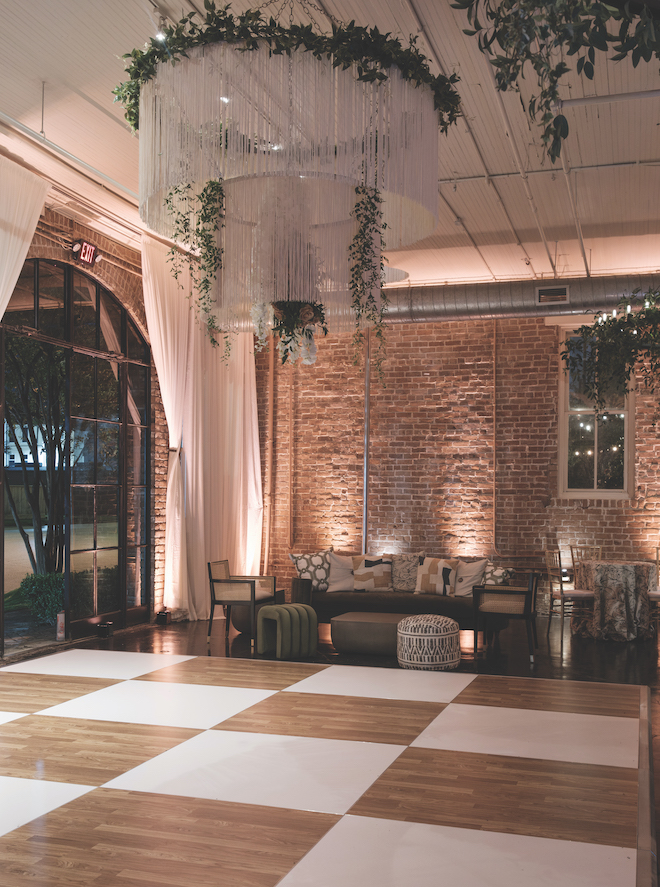 Low lit dance floor with rope chandelier adorned with greenery.