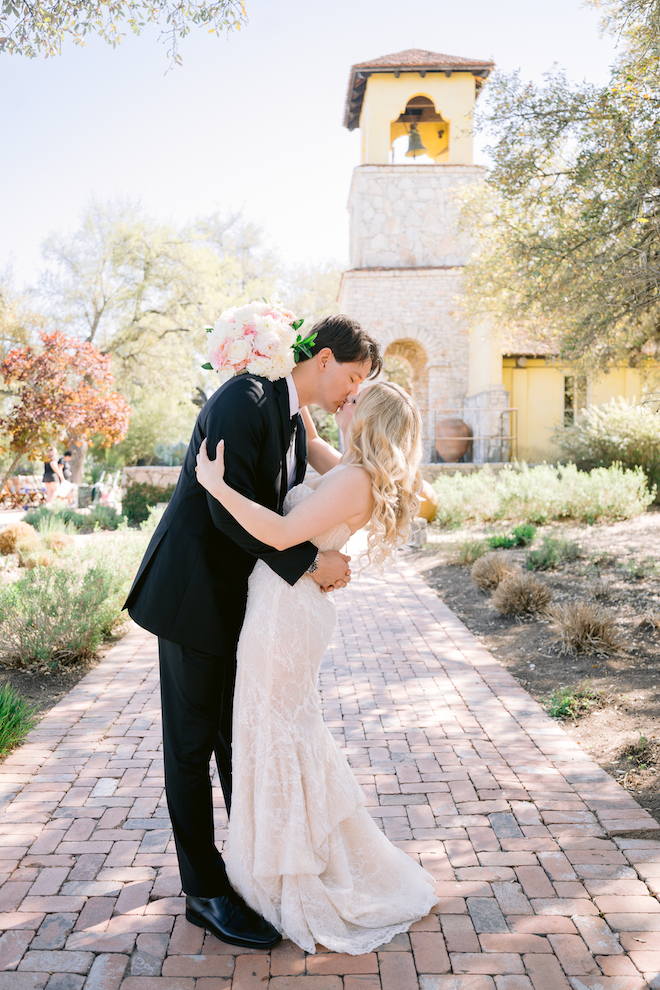 Newlyweds kissing on brick sidewalk after Texas hill country wedding.