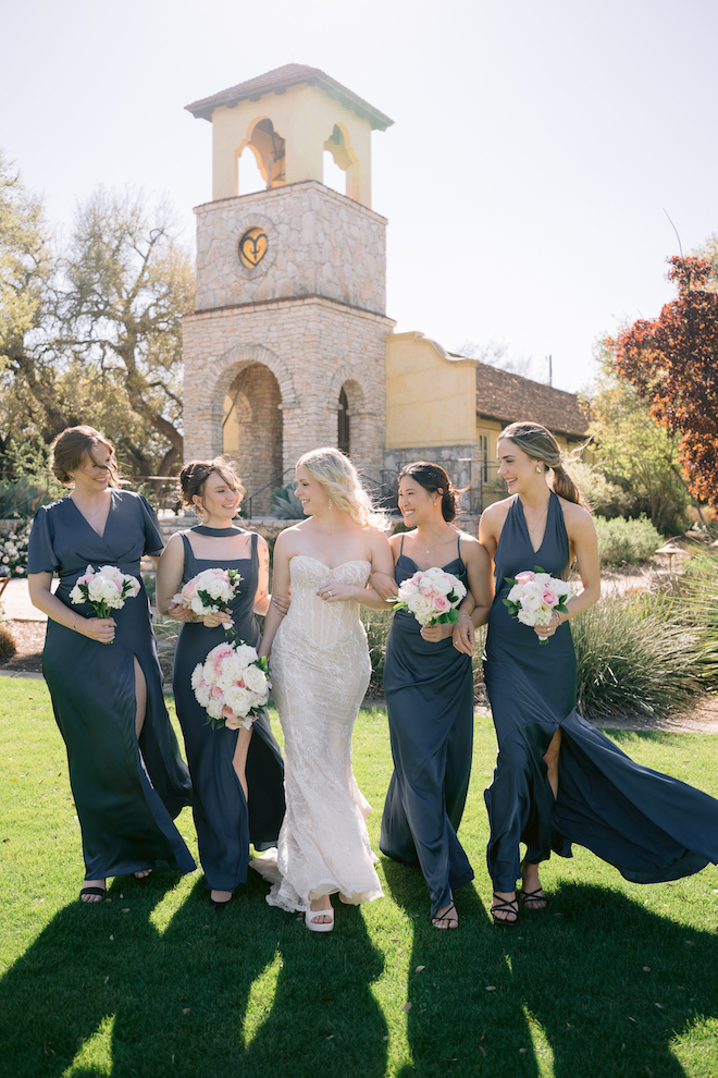 Bride and bridesmaids in dark blue walking together before intimate Hill Country wedding.