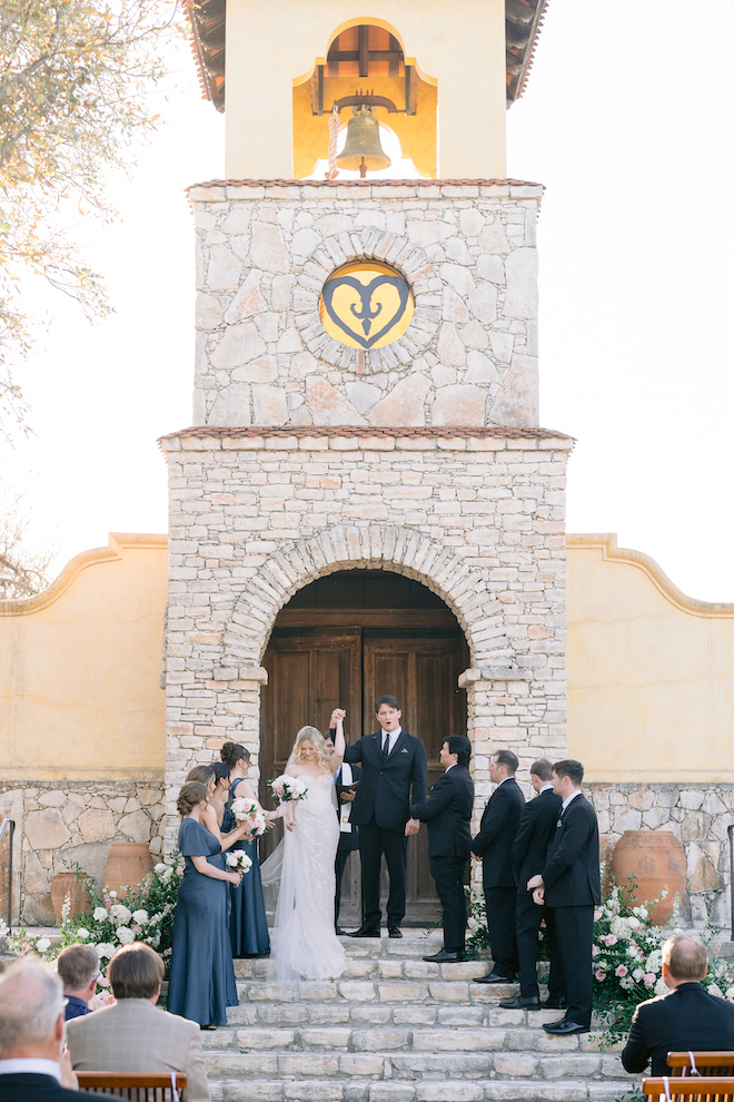 Bride and groom cheering at the altar in front of stone church.