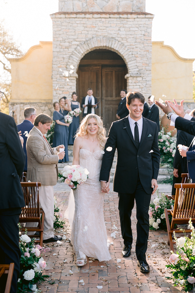 Bride and groom walking down the aisle together as guests throw rose petals.
