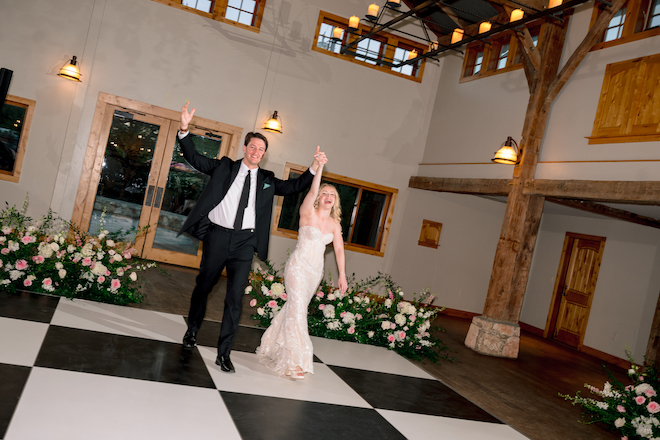 Bride and groom walking in to reception together on black and white checkered dance floor.