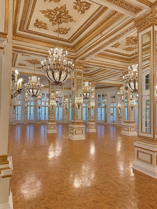 Elegant grand ballroom with gold details accenting the ceiling, chandeliers, and pillars.
