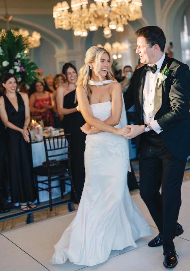 The couple hold hands as they dance at their wedding reception as guests watch. 