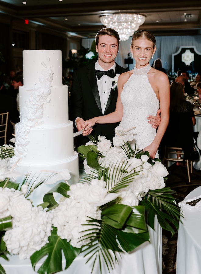 The couple smile as they cut into their seashell-inspired wedding cake by Cakes by Gina.