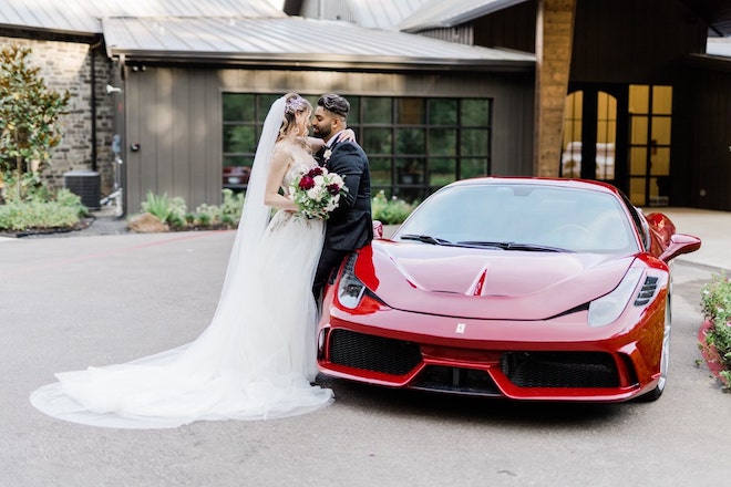 Newlyweds standing next to red sports car for luxury wedding details outside of venue.