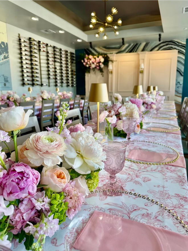 White and purple flowers as centerpieces along long running table. 