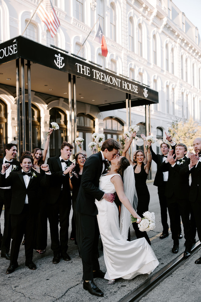 Bride and groom kissing while wedding party cheers behind them.