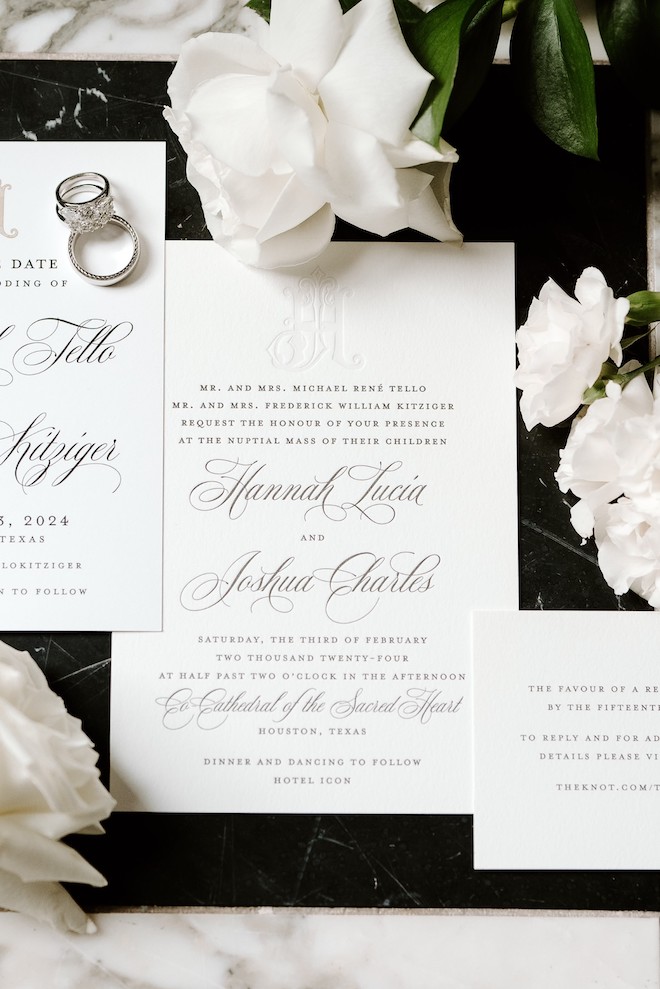 White wedding invitations with cursive calligraphy on it surrounded by white florals.