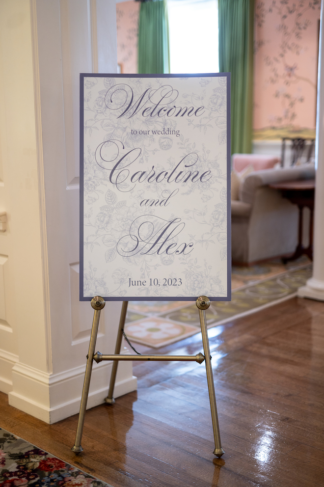 Blue and white detailed welcome sign on easel that reads, "Welcome to our wedding Caroline and Alex, June 10, 2023"