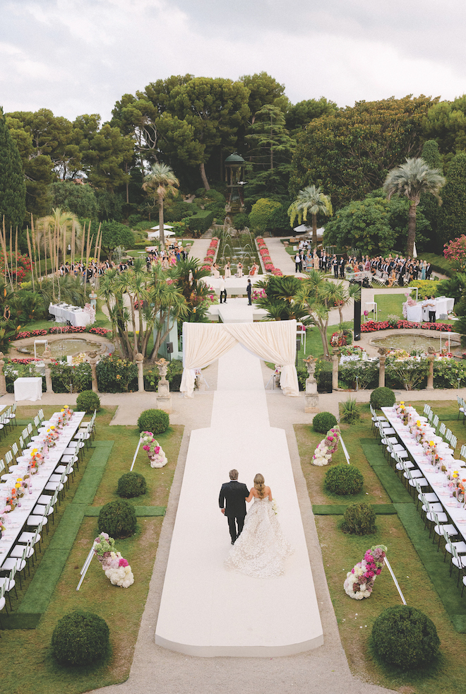 Aerial shot of bride and father of the bride walking down the aisle in the middle of the French Riviera with colorful details.