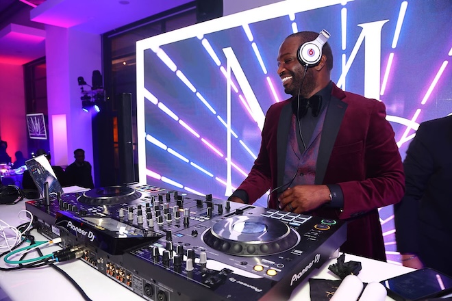 A DJ plays at a wedding reception in front a bright light up sign. 