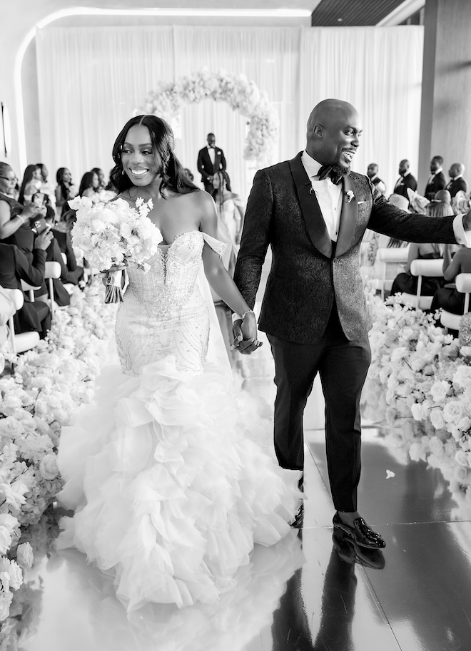 The bride and groom hold hands as they walk down the aisle at their ceremony. 