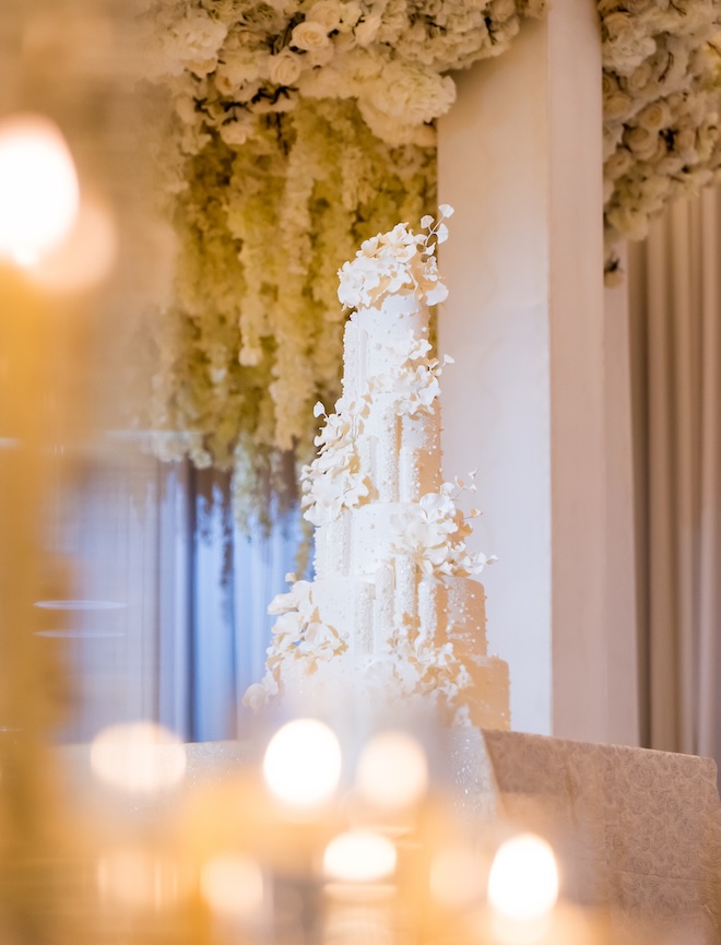 A six-tier wedding cake embellished in white floral is the focal point of the reception. 