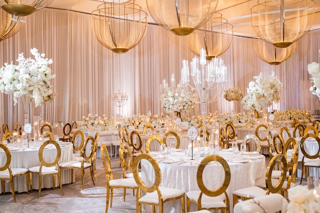 Gold chairs, white florals and candles decorate the reception tables. 