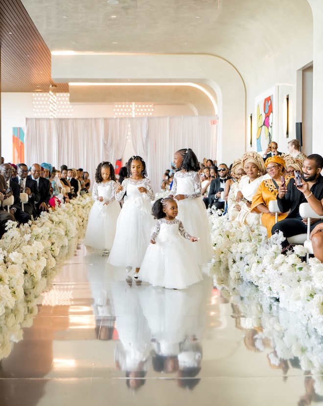 Four flower girls walk down a mirrored aisle at the wedding ceremony.