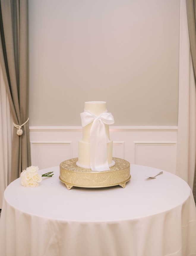 A three-tier wedding cake is tied with a white bow. 