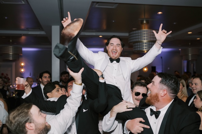 The groom is lifted in the air by wedding guests at the reception. 
