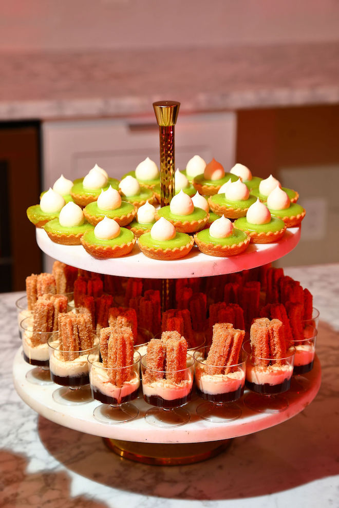 Small green treats with churro treats beneath them on a two tier plate platter.