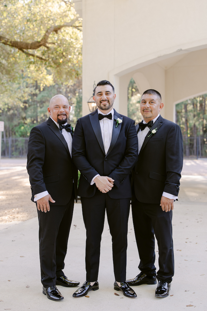 Groom standing with two groomsmen outside of wedding venue.
