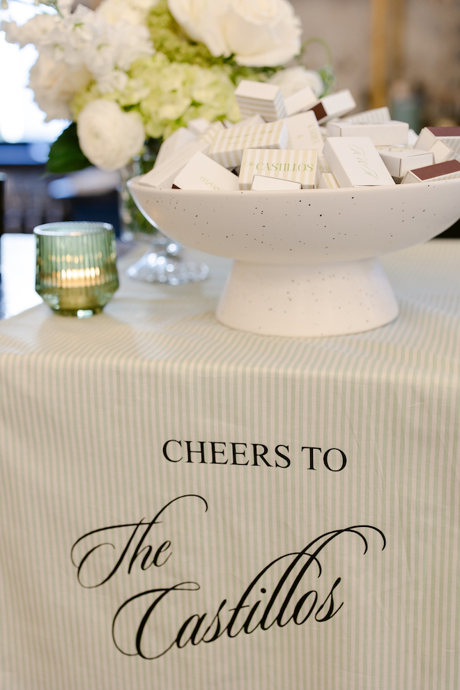 Table with linen that reads "Cheers to The Castillos" with a white bowl filled with matchboxes.