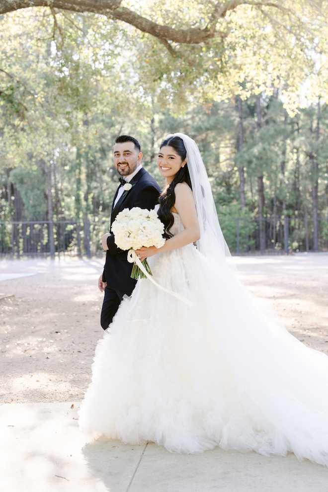 Bride and groom walking and smiling together surrounded by trees.