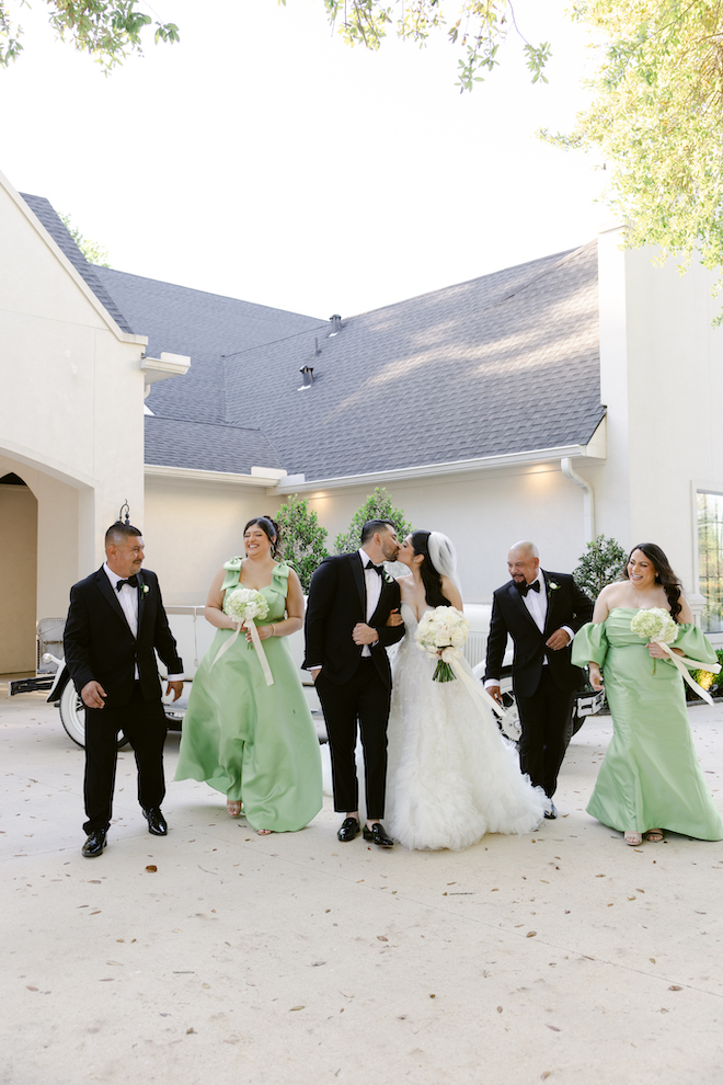 Bride and groom kissing outside of venue with groomsmen and bridesmaids.