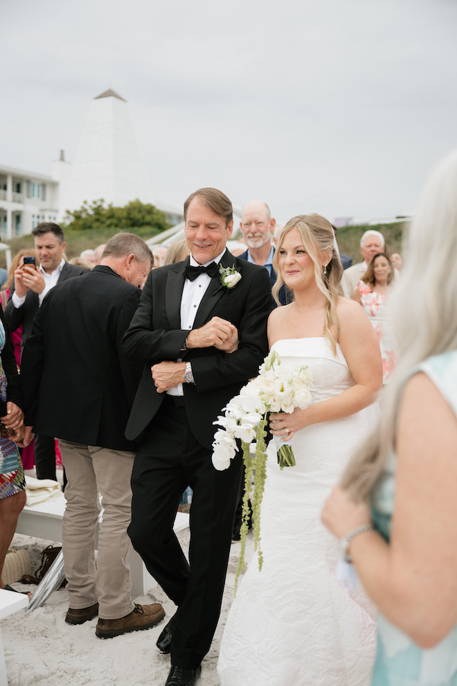 Bride walking down the sandy aisle with her father in her intimate Seaside wedding.