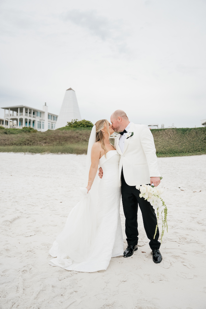 Newlyweds kissing on the beach in front of the white Seaside tower.