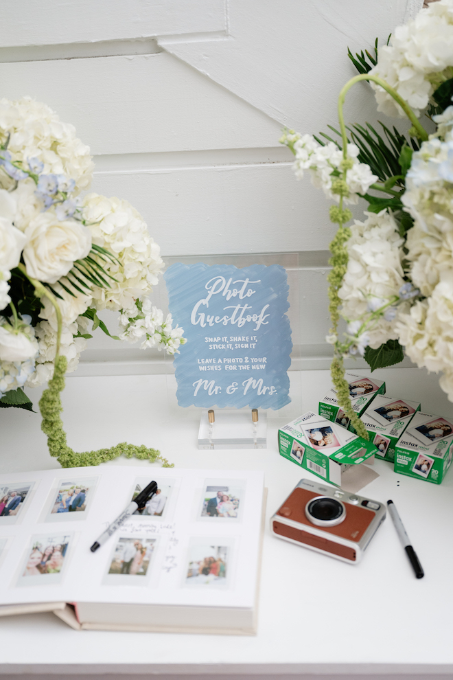 Photo guestbook station with polaroid cameras and white and light blue bouquets.