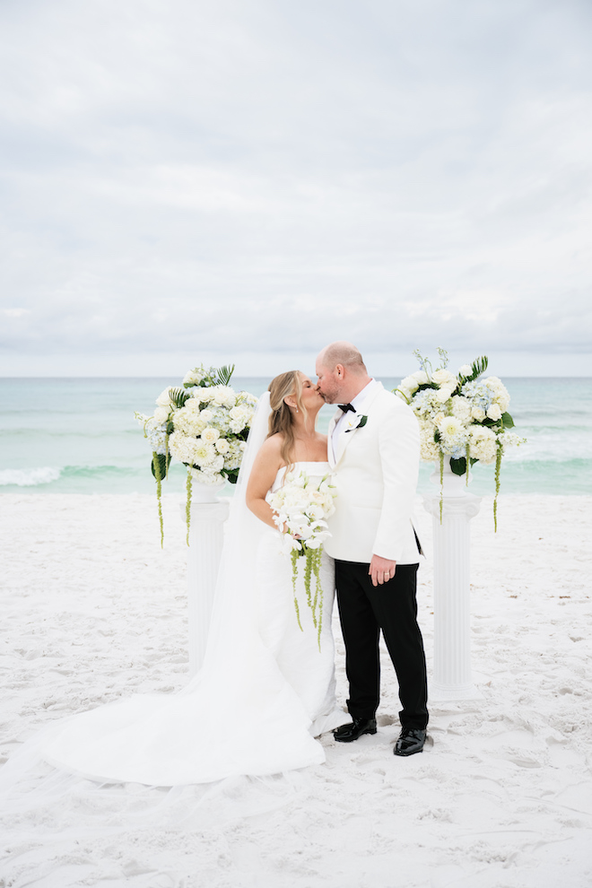 Newlyweds kissing on the beach in front of the altar with the ocean behind them.