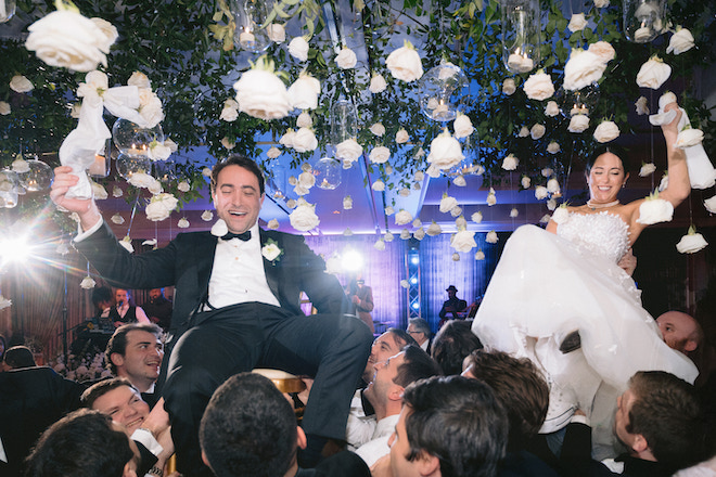Bride and groom being lifted in the air  in chairs by guests.