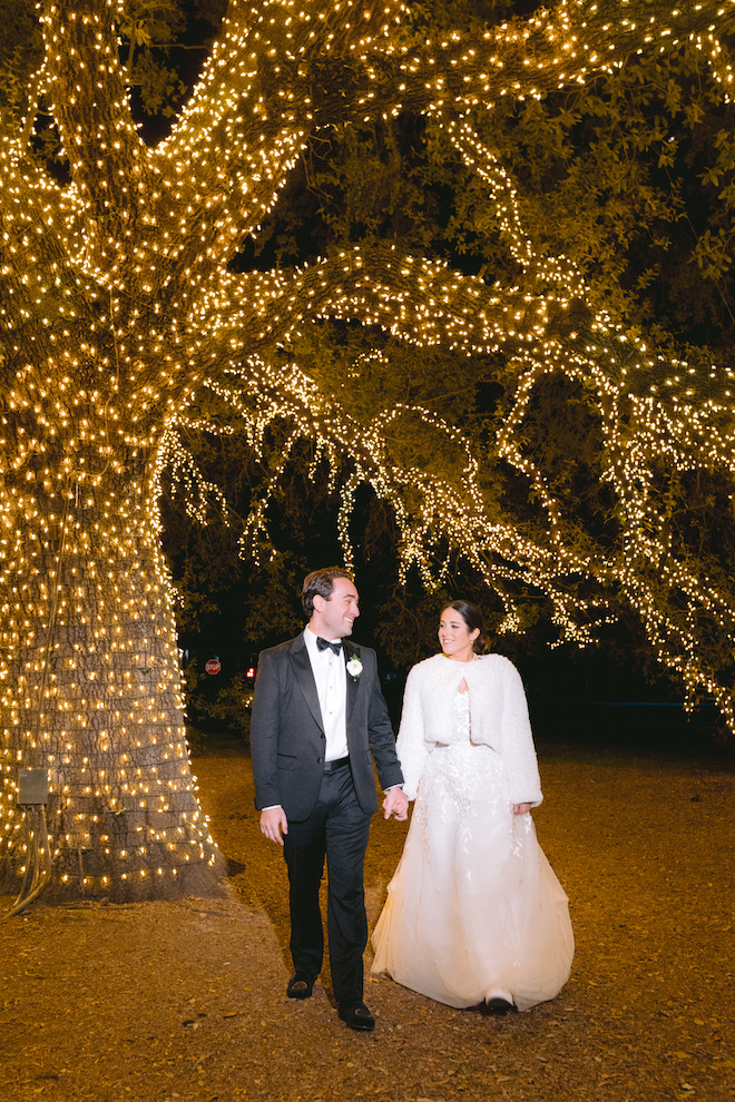 Newlyweds walking together under Houstonian oak tree lit up by mini fairy lights.