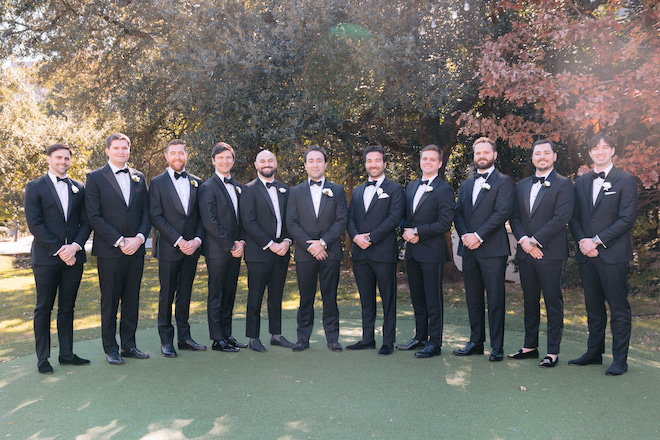 Groomsmen in tuxes on turf.