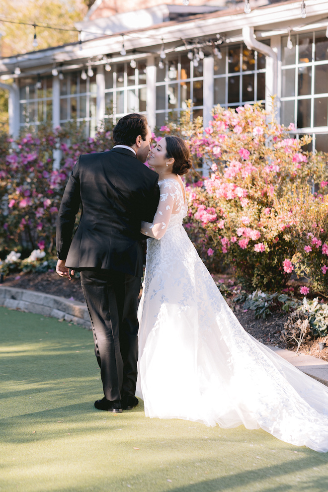 Newlyweds walking away next to pink floral bushes.