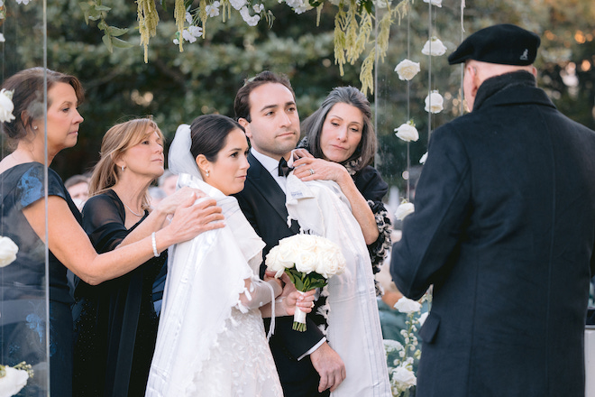 Bride and groom at the chuppah performing a Jewish tradition with family behind them.