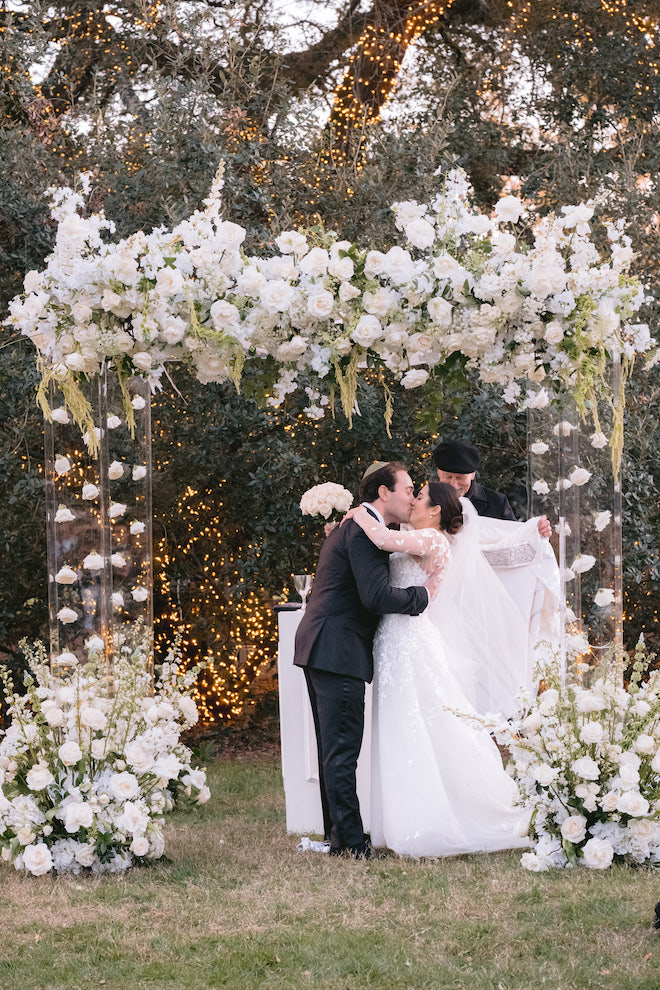 Bride and groom kissing under the floral adorned chuppah.