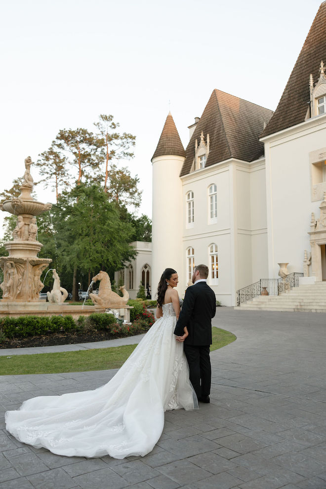 Bride and groom holding hands outside of venue next to big water fountain.
