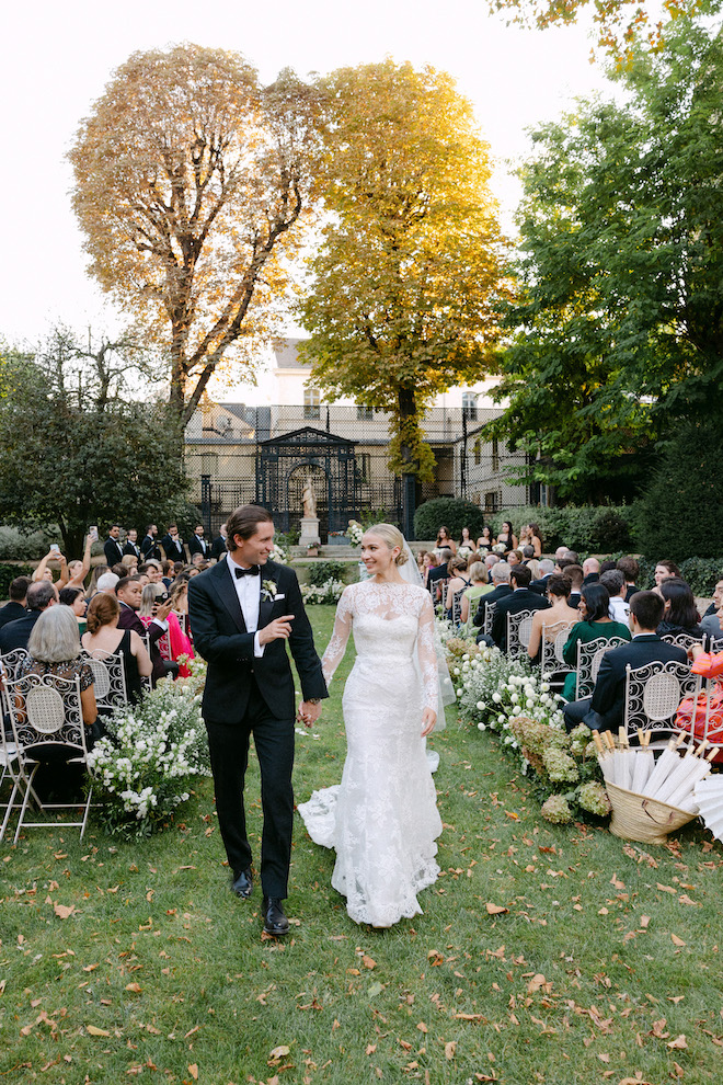 Newlyweds walking down a grass outdoor aisle in their Pairs wedding. 