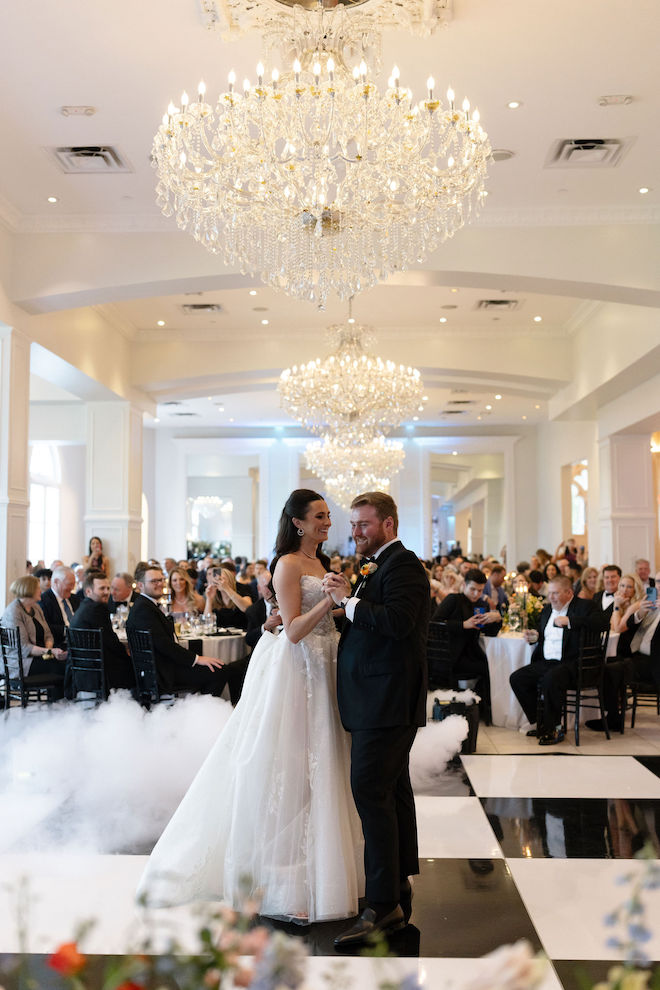 The couple dancing on the black-and-white checkered dance floor in front of the guests.