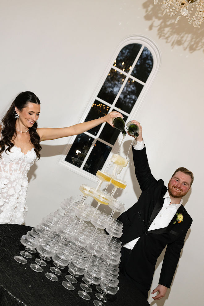 Bride and groom pouring champagne into a stacked champagne tower.
