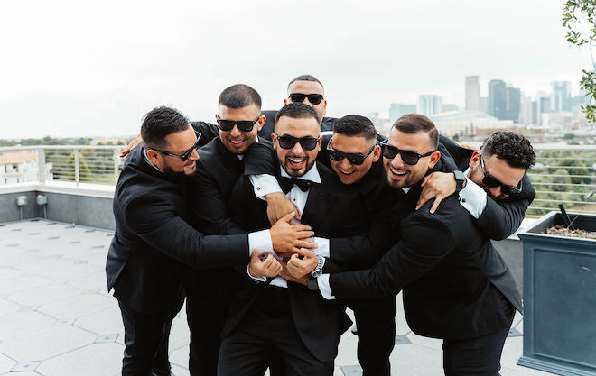 Groomsmen all hugging the groom in front of Houston skyline.