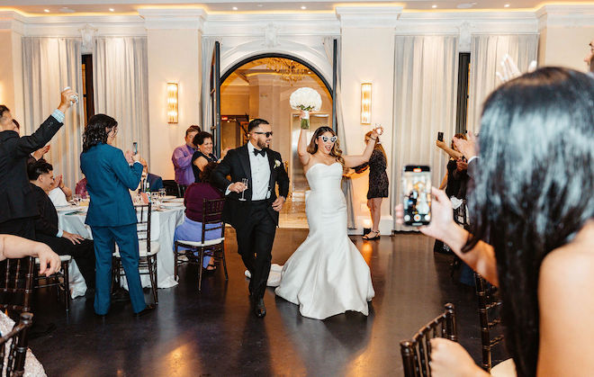 The newlyweds walking and cheering into their reception with guests supporting around them.